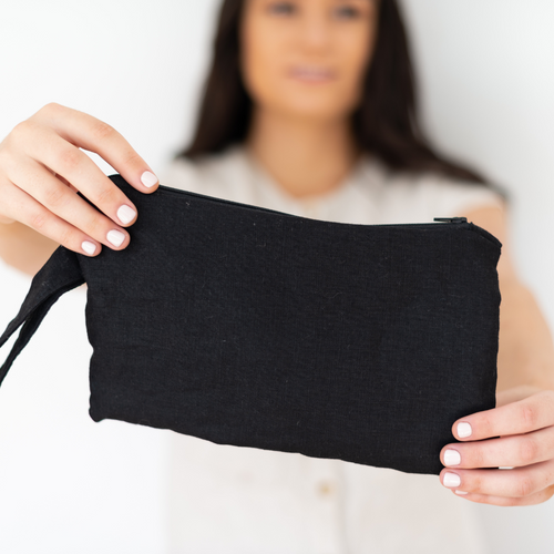 Black linen clutch in foreground, held by a young brunette lady in the background 