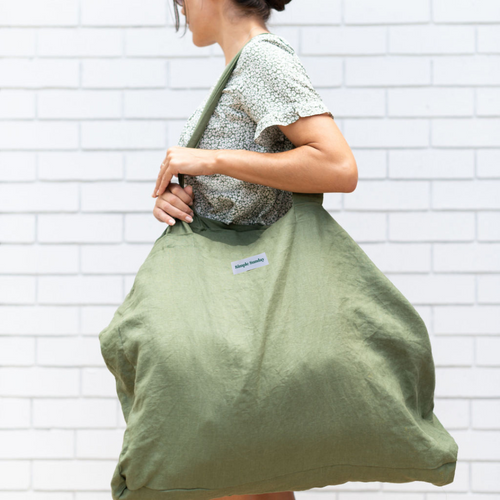brunette lady holding large olive green 100% linen, Australian Made beach bag against white brick wall