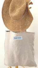 Load image into Gallery viewer, Stone coloured 100% linen, Australian made  tote bag handing on wooden hat rack with cane hat
